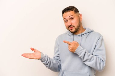 Beyaz arka planda izole edilmiş genç İspanyol bir adam heyecanlı bir şekilde avuç içinin bir kopyasını tutuyor..