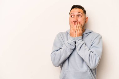 Genç İspanyol bir adam beyaz arka planda izole edilmiş. Düşünceli bir şekilde bir fotokopi odasına bakıyor. Ağzını eliyle kapatıyor..