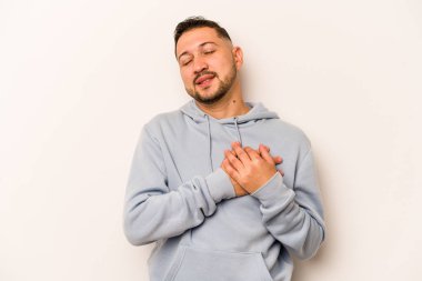 Beyaz arka planda izole edilmiş genç İspanyol bir adam, dost canlısı bir ifadeye sahip, avuçlarını göğsüne bastırıyor. Aşk konsepti.