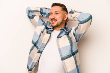 Beyaz arka planda izole edilmiş genç İspanyol bir adam kendini güvende hissediyor, elleri başının arkasında..