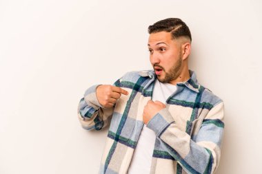 Beyaz arka planda izole edilmiş genç İspanyol adam parmağını göstererek şaşırdı, geniş bir gülümsemeyle..