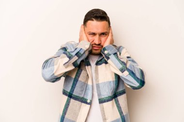 Beyaz arka planda izole edilmiş genç İspanyol adam kulaklarını elleriyle kapatıyor..