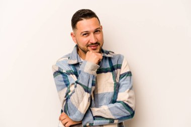 Beyaz arka planda izole olmuş genç İspanyol adam gülümsüyor ve kendinden emin, elleriyle çeneye dokunuyor..