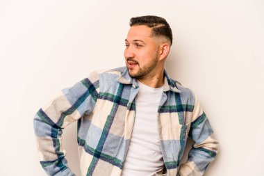 Beyaz arka planda izole edilmiş genç İspanyol adam mutlu bir şekilde gülüyor ve ellerini karnının üstünde tutarak eğleniyor..