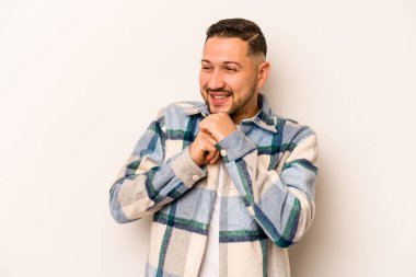 Beyaz arka planda izole edilmiş genç İspanyol adam ellerini çenesinin altında tutuyor ve mutlu bir şekilde yan tarafa bakıyor..