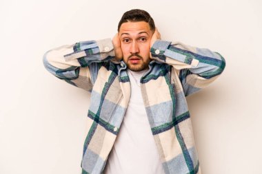 Latin kökenli genç adam beyaz arka planda izole edilmiş. Kulakları kulaklarıyla kapatıyor. Çok fazla ses duymamaya çalışıyor..