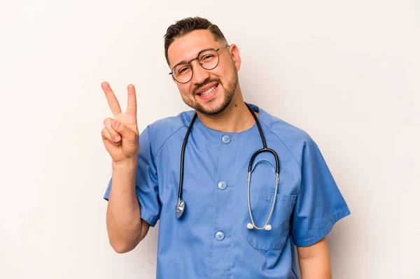 白い背景に孤立したヒスパニック看護師の男喜びと屈託のない指で平和のシンボルを示す — ストック写真