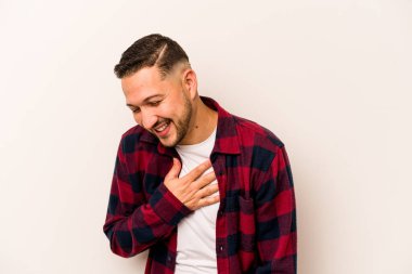 Beyaz arka planda izole olmuş genç İspanyol adam gülüyor, elleri yüreğinde, mutluluk kavramında..