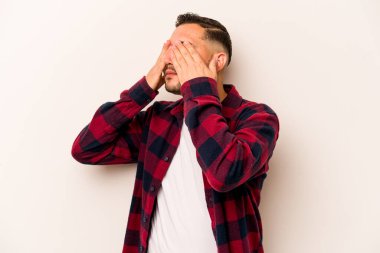 Beyaz arka planda izole edilmiş genç İspanyol adam elleriyle gözlerini kapatmaktan korkuyor..