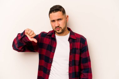 Beyaz arka planda izole edilmiş genç İspanyol adam baş parmağını aşağı gösteriyor, hayal kırıklığı konsepti..