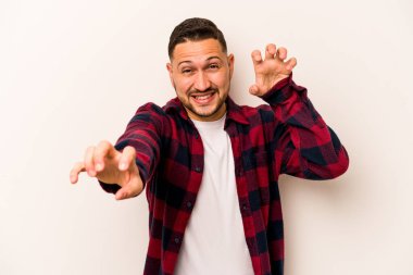 Beyaz arka planda izole edilmiş genç İspanyol bir adam pençelerini bir kediyi taklit ederken gösteriyor, agresif bir hareket..