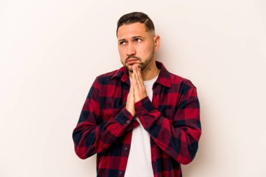 Latin kökenli genç bir adam beyaz arka planda izole edilmiş dua ediyor, bağlılık gösteriyor, dindar biri ilahi ilham arıyor..