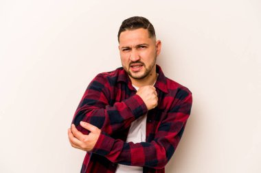 Genç İspanyol bir adam beyaz arka planda izole edilmiş, dirsek masajı yapıyor, kötü bir hareketin ardından acı çekiyor..