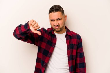 Beyaz arka planda izole edilmiş genç İspanyol adam baş parmağını aşağı gösteriyor ve hoşlanmadığını ifade ediyor..