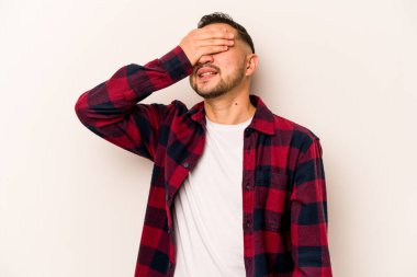 Beyaz arka planda izole edilmiş genç İspanyol adam elleriyle gözlerini kapatıyor, geniş bir gülümsemeyle bir sürpriz bekliyor..