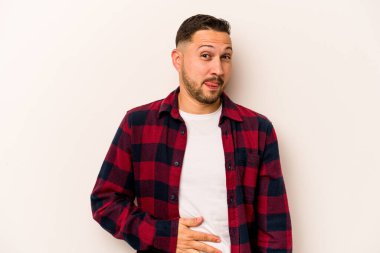 Beyaz arka planda izole edilmiş genç İspanyol adam karnına dokunuyor, nazikçe gülümsüyor, yemek yiyor ve tatmin oluyor..