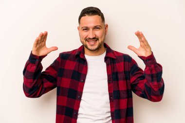 Beyaz arka planda izole edilmiş genç İspanyol bir adam avuçlarıyla bir şey tutuyor ve kameraya sunuyor..