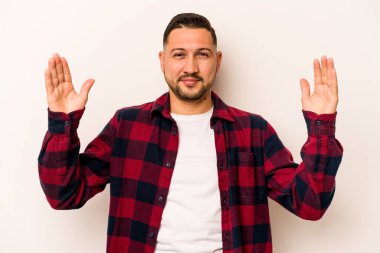 Beyaz arka planda izole edilmiş genç İspanyol adam işaret parmaklarıyla küçük bir şey tutuyor, gülümsüyor ve kendinden emin..