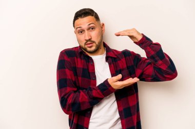 Beyaz arka planda izole edilmiş genç İspanyol adam iki eliyle bir şey tutuyor, ürün sunumu..