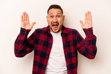Latin kökenli genç bir adam beyaz arka planda izole edilmiş. Hoş bir sürprizle karşılaşıyor, heyecanlı ve el kaldırıyor..