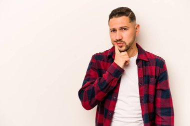 Beyaz arka planda izole edilmiş genç bir İspanyol şüpheli ve şüpheci bir ifadeyle yana bakıyor..
