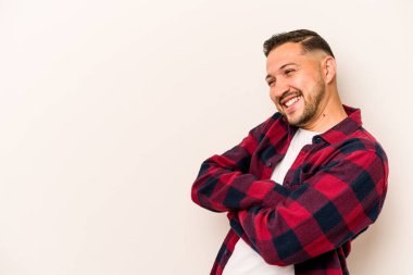 Beyaz arka planda izole edilmiş genç İspanyol adam kollarını kavuşturarak gülümsüyor..