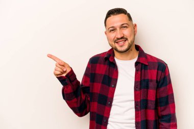 Beyaz arka planda izole edilmiş genç İspanyol adam işaret parmağıyla işaret ederek gülümsüyor..