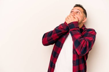 Genç İspanyol bir adam beyaz arka planda izole edilmiş. Düşünceli bir şekilde bir fotokopi odasına bakıyor. Ağzını eliyle kapatıyor..