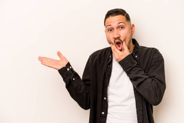 Beyaz arka planda izole edilmiş genç İspanyol bir adam avuç içinde fotokopi alanı tutuyor, el üstünde tutuyor. Şaşırmış ve mutlu..