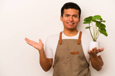 Genç bahçıvan İspanyol arka planda izole edilmiş bir bitki tutuyor. Bir avuç içinde fotokopi alanı ve belinde başka bir el tutuyor..