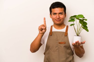 Genç bahçıvan İspanyol bir bitki tutuyor. Beyaz arka planda bir numarayı parmağıyla gösteriyor..