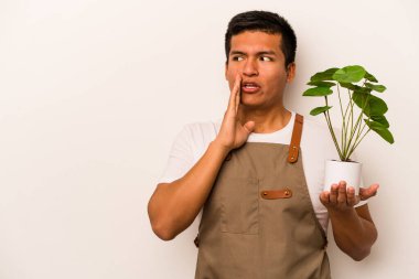 Beyaz arka planda izole edilmiş bir bitki tutan genç bahçıvan gizli bir sıcak fren haberinin olduğunu söylüyor.