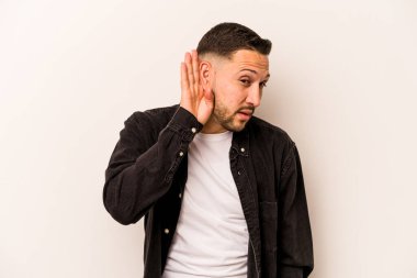 Latin kökenli genç bir adam beyaz arka planda bir dedikoduyu dinlemeye çalışıyor..