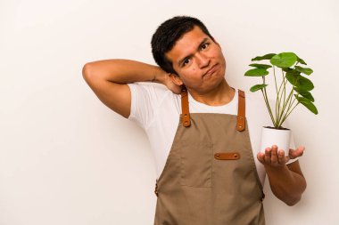 Genç bahçıvan İspanyol bir bitki tutuyor. Beyaz arka planda izole edilmiş. Kafasının arkasına dokunuyor, düşünüyor ve bir seçim yapıyor..