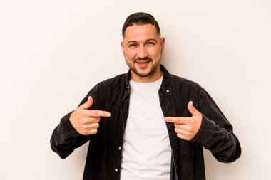 Beyaz arka planda izole edilmiş genç bir İspanyol gömlek fotokopi alanını elle işaret ediyor, gururlu ve kendinden emin.