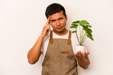 Genç bahçıvan, beyaz arka planda bir bitki tutuyor. Şakağı işaret ediyor, düşünüyor, bir göreve odaklanıyor..