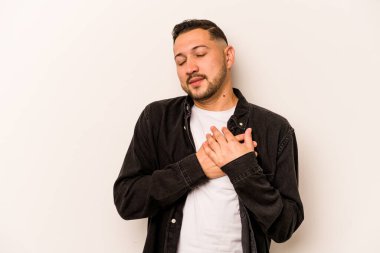 Beyaz arka planda izole edilmiş genç İspanyol bir adam, dost canlısı bir ifadeye sahip, avuçlarını göğsüne bastırıyor. Aşk konsepti.