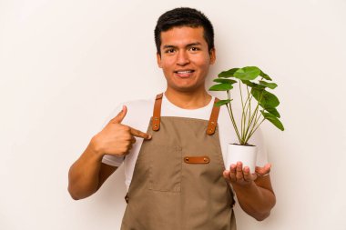 Genç bahçıvan, beyaz arka plandaki bir bitkiyi elinde tutuyor. Elle bir tişört fotokopi alanını işaret ediyor, gururlu ve kendinden emin.