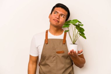 Genç bahçıvan İspanyol asıllı bir adam beyaz arka planda bir bitki tutuyor. Amaçlarına ve amaçlarına ulaşma hayalleri kuruyor.