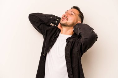 Beyaz arka planda izole edilmiş genç İspanyol bir adam kendini güvende hissediyor, elleri başının arkasında..