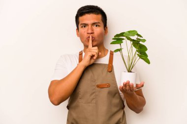 Genç bahçıvan İspanyol bir adam beyaz arka planda bir bitki tutuyor ya sır saklıyor ya da sessizlik istiyor..
