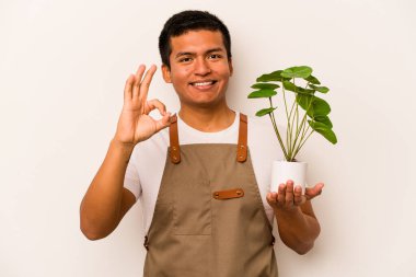 Genç bahçıvan İspanyol bir bitki tutuyor. Beyaz arka planda izole edilmiş. Neşeli ve kendinden emin..