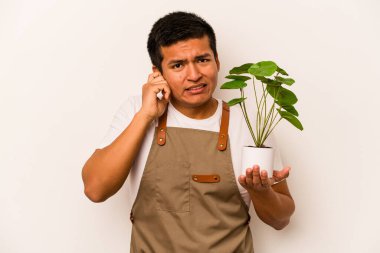 Genç bahçıvan İspanyol bir bitki tutuyor. Beyaz arka planda izole edilmiş. Kulakları elleriyle kapatıyor..