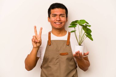Genç bahçıvan İspanyol bir bitki tutuyor. Beyaz arka planda iki numarayı parmaklarıyla gösteriyor..