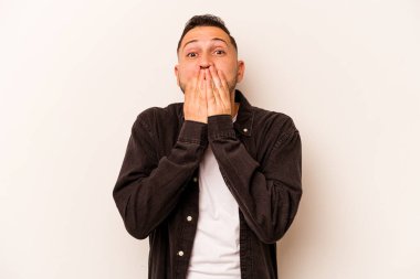 Beyaz arka planda izole edilmiş genç İspanyol adam elleriyle ağzını kapatırken şok oldu..