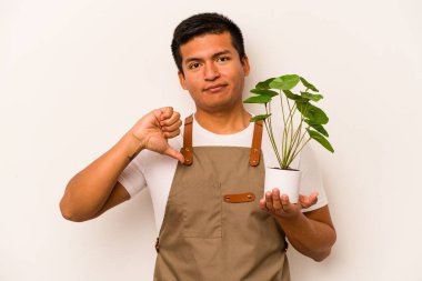 Genç bahçıvan İspanyol bir adam beyaz arka planda izole edilmiş bir bitki tutuyor. Sevimsiz bir jest gösteriyor. Anlaşmazlık konsepti.