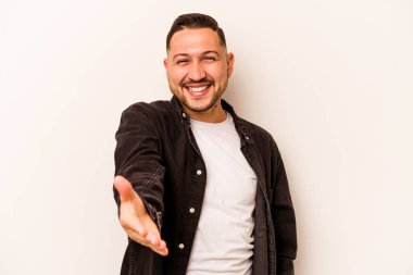 Beyaz arka planda izole edilmiş genç İspanyol adam selamlama jesti olarak kameraya elini uzatıyor..