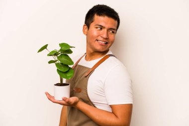 Genç bahçıvan İspanyol arka planda izole edilmiş bir bitki tutuyor. Gülümsüyor, neşeli ve keyifli..