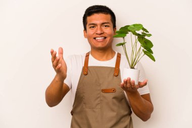 Genç bahçıvan İspanyol asıllı bir adam beyaz arka planda bir bitki tutuyor. Hoş bir sürprizle karşılaşıyor, heyecanlı ve el kaldırıyor..