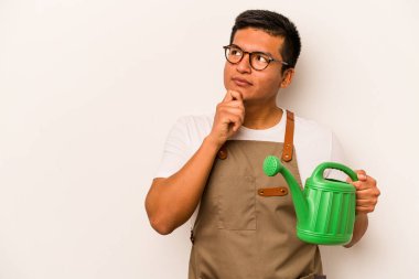 Genç bahçıvan, elinde su dolu bir teneke kutu tutan, şüpheli ve şüpheci bir ifadeyle beyaz arka plana bakan bir İspanyol..